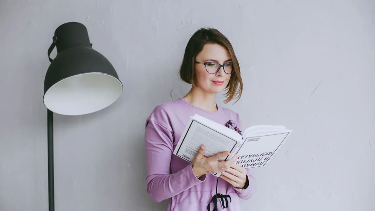 Женская анатомия: как всё устроено, от вульвы до тазового дна. a woman standing next to a lamp reading a book Фото: Julia Potter, Unsplash